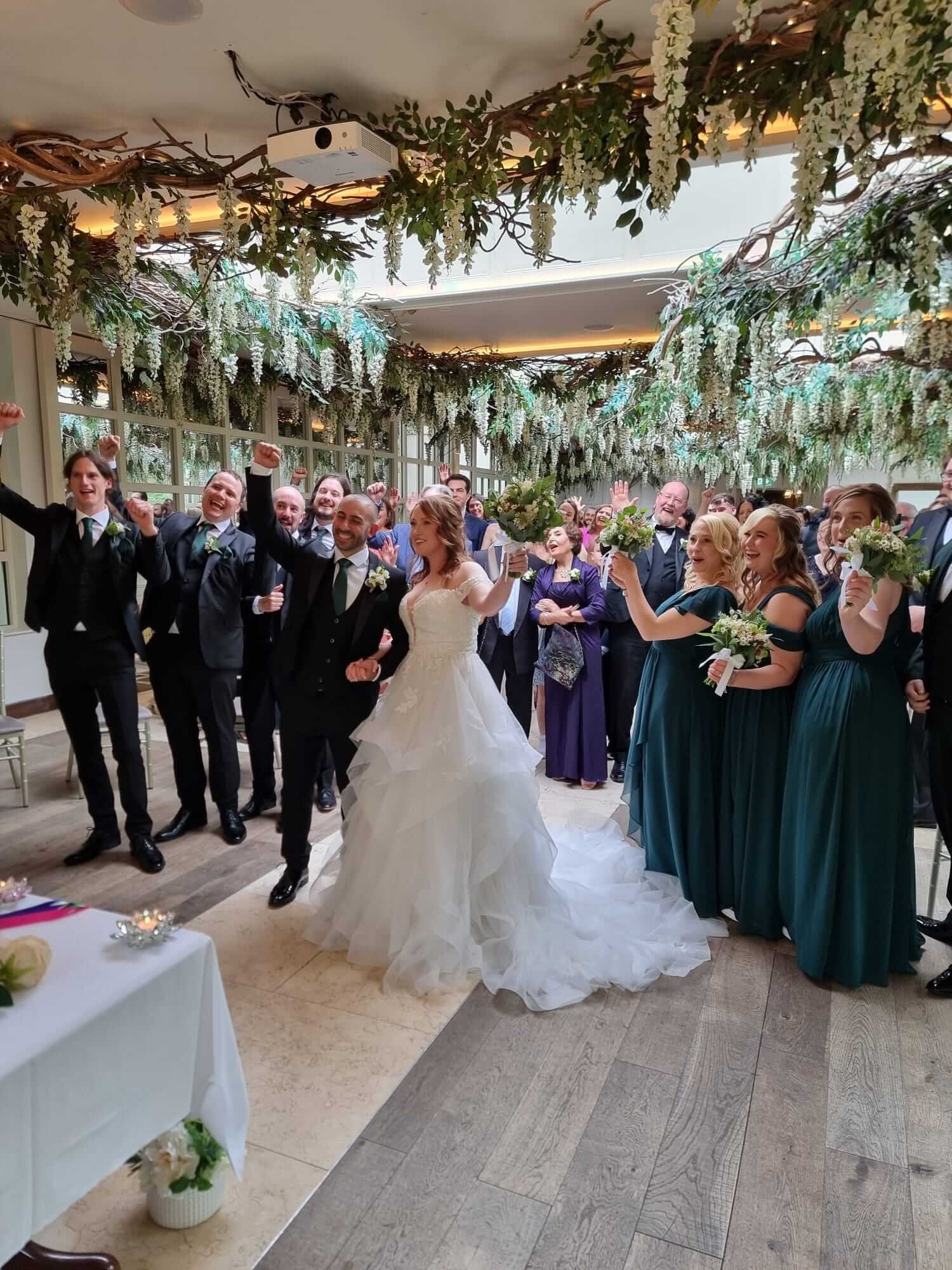 Happy newlyweds Omid & Stephanie recessing down the aisle at a Maryborough Hotel wedding, surrounded by celebrating guests and lush greenery decor.