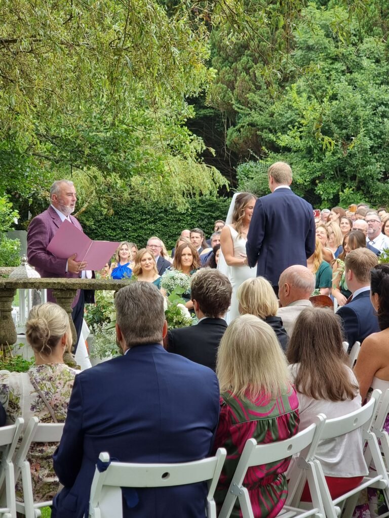 Outdoor wedding ceremony at Inishannon House Hotel with the bride and groom exchanging vows, guided by the celebrant, surrounded by guests.